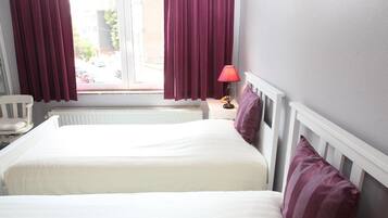 Een hotelkamer met twee bedden, een raam met gordijnen, een nachtkastje met een lamp en een stoel.
