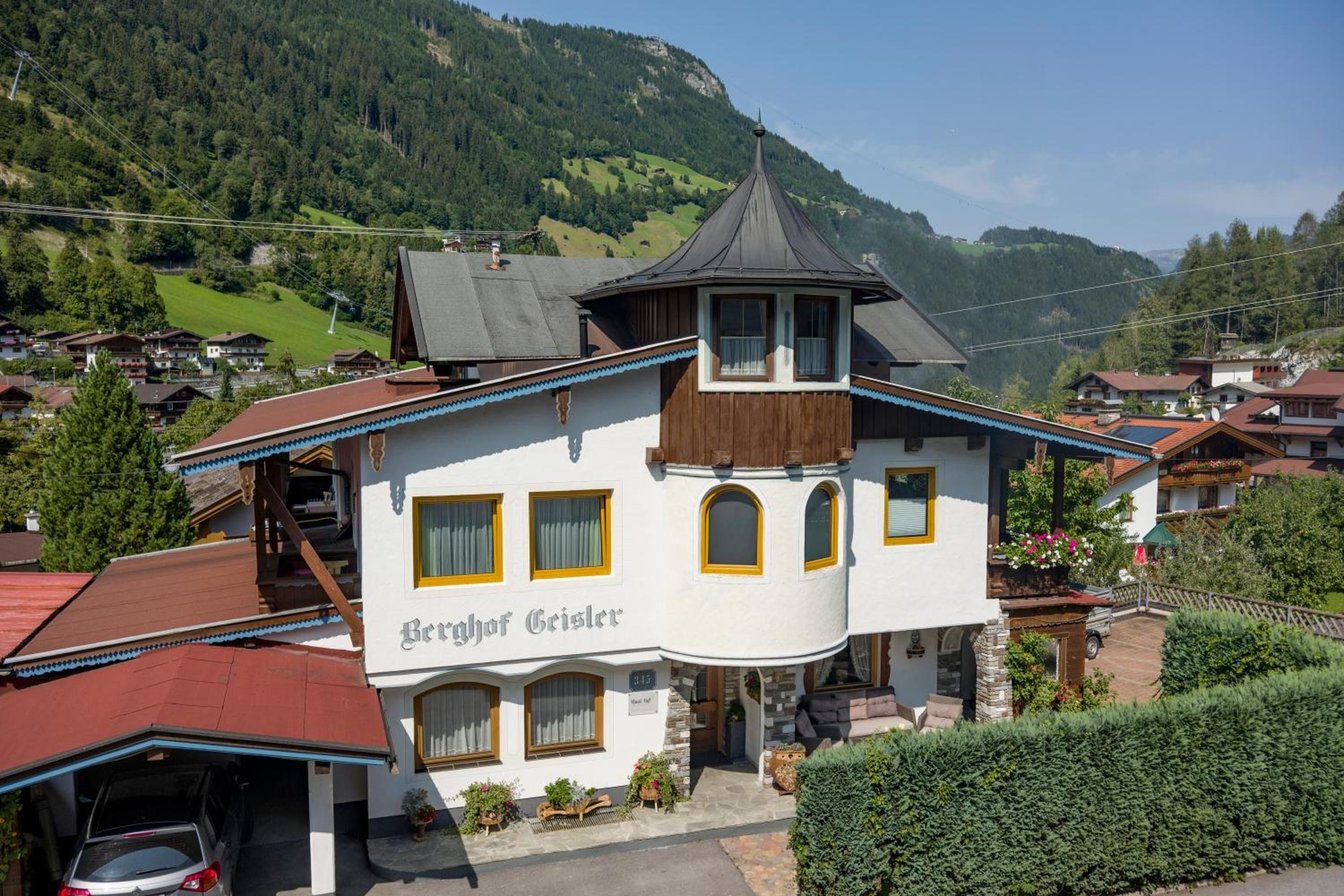 A two-story building with a prominent tower, labeled 'Berghof Geisler,' surrounded by a mountainous landscape.