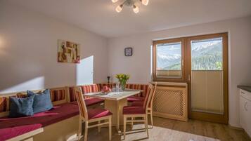 A cozy room with a wooden bench seating area, a dining table with chairs, a clock on the wall, and a window with a mountain view.