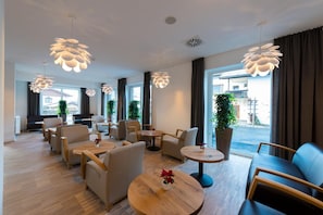Un hall d’hôtel doté de meubles modernes, de grandes fenêtres et de luminaires décoratifs au plafond.