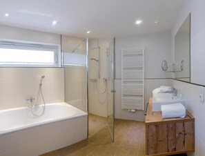 Une salle de bain moderne avec une douche à parois de verre, une baignoire sur pieds et un meuble-lavabo en bois doté d’un miroir.