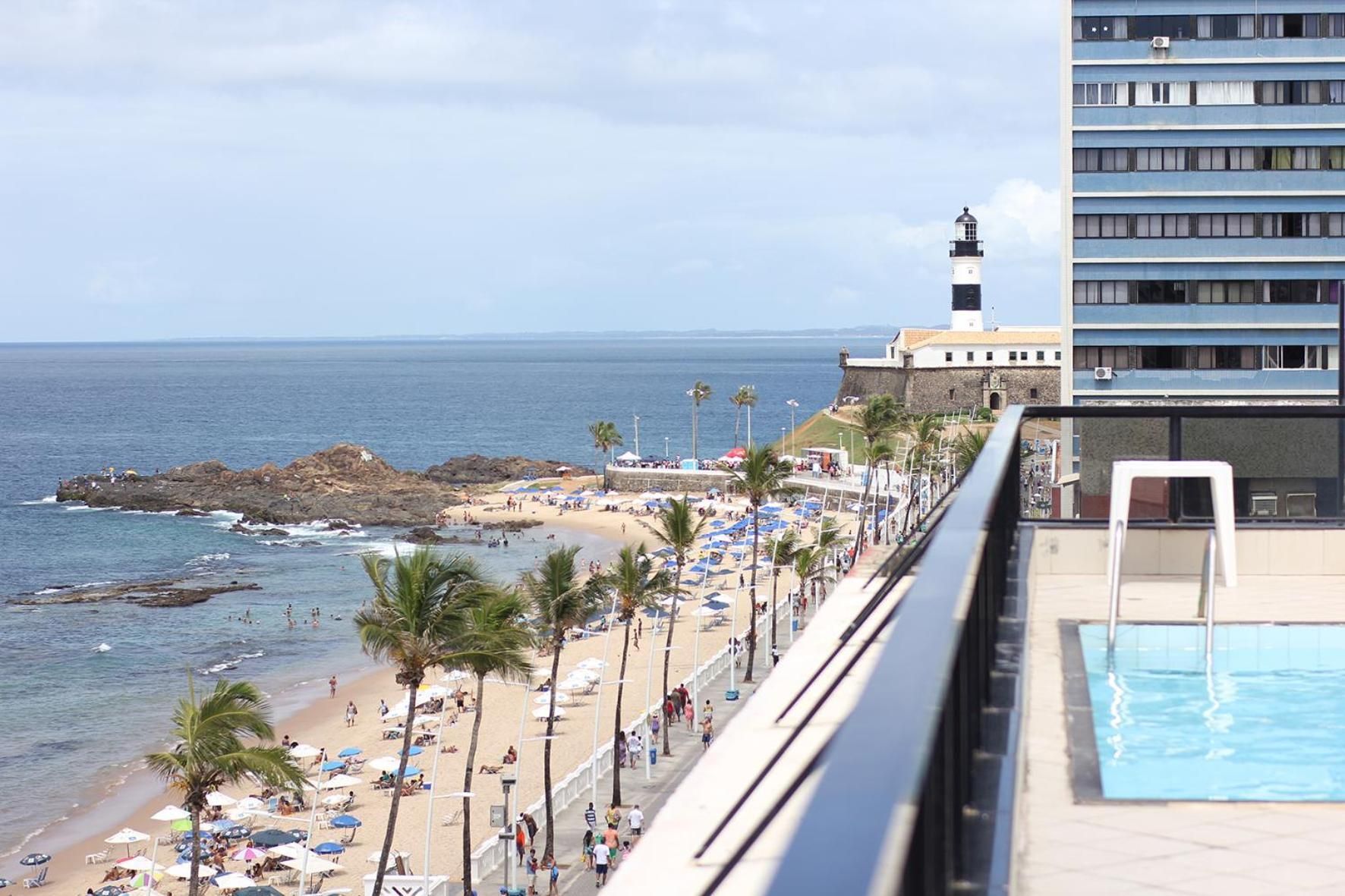 Una playa con piscina, un faro y un edificio con balcones con vista al océano.