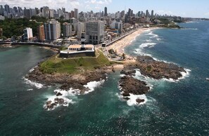 Vista aérea de una ciudad costera con una isla rocosa destacada y un moderno complejo de edificios.