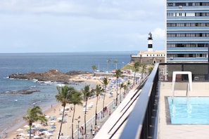 Una playa con piscina, un faro y un edificio con balcones con vista al océano.
