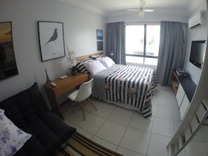 Habitación de hotel con cama, escritorio, silla, televisión y ventana con cortinas.