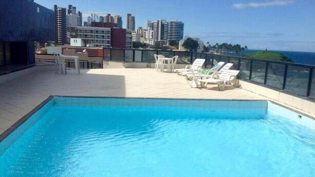 A rooftop swimming pool with lounge chairs and a cityscape view. - Flat Farol Da Barra (Salvador)