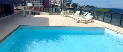 A rooftop swimming pool with lounge chairs and a cityscape view.