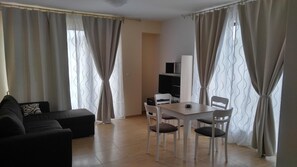 A living room with a sofa, a dining table with chairs, and a TV. - Boulevard Sea Residence (Nessebar)