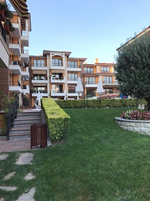 A multi-story residential building with balconies, a well-maintained lawn, and outdoor seating areas. - Boulevard Sea Residence (Nessebar)