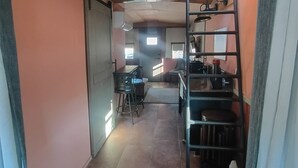 Um corredor estreito com escada que leva a um andar superior, área de cozinha com pia e fogão, e área de jantar com cadeiras e mesa.