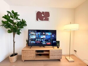 Ein Fernseher auf einem Holzboden, mit einer Pflanze links und einer Lampe rechts.