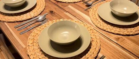 A dining table set with woven placemats, bowls, and cutlery.