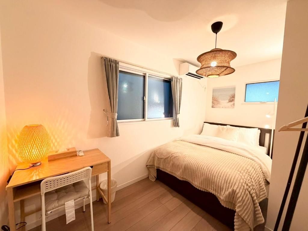 Een slaapkamer met een bed, een bureau, een stoel, een raam met gordijnen en een hanglamp.