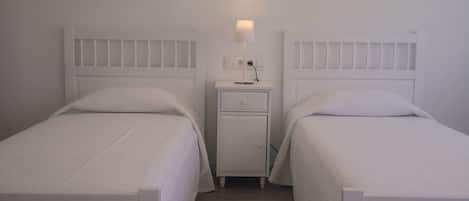 A room with two single beds, a bedside table with a lamp, and a wall-mounted light fixture.