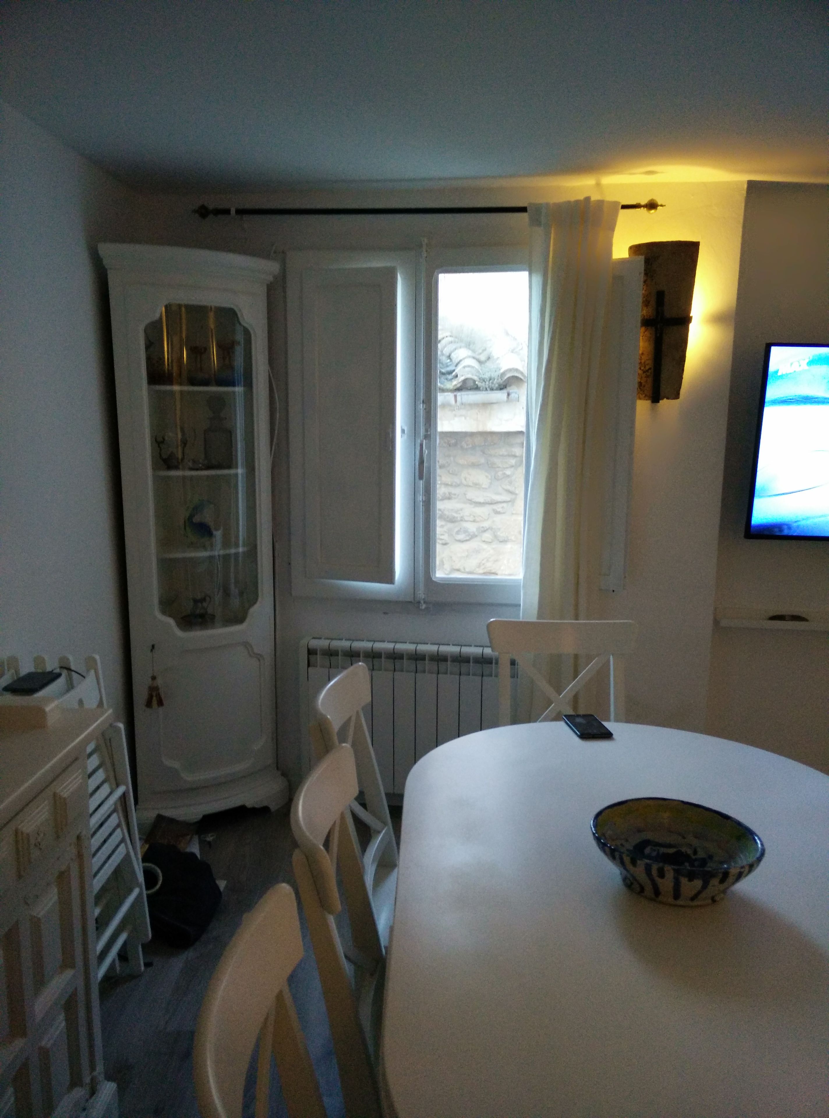 A room with a dining table, chairs, a television, a window with curtains, and a radiator.