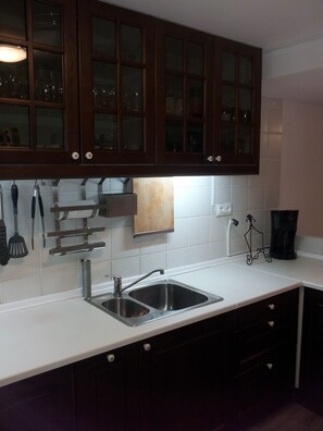 Cocina con armarios de madera oscura, pileta de acero inoxidable y salpicadero de azulejos blancos.