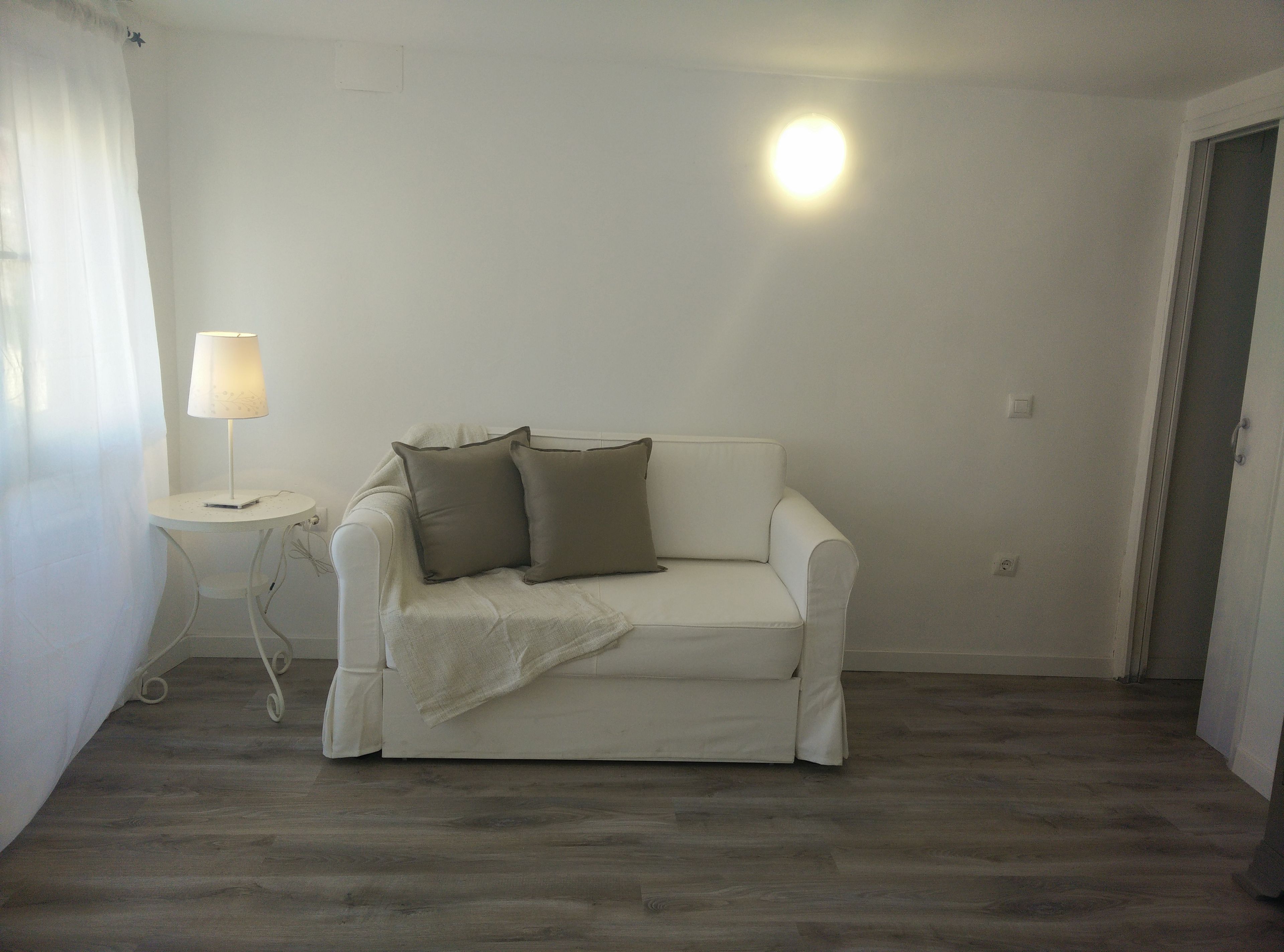 Un sofá blanco con dos almohadas, una mesita con una lámpara y un accesorio de iluminación en el techo.