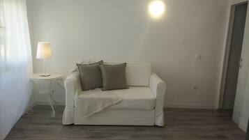 Un sofá blanco con dos almohadas, una mesita con una lámpara y un accesorio de iluminación en el techo.