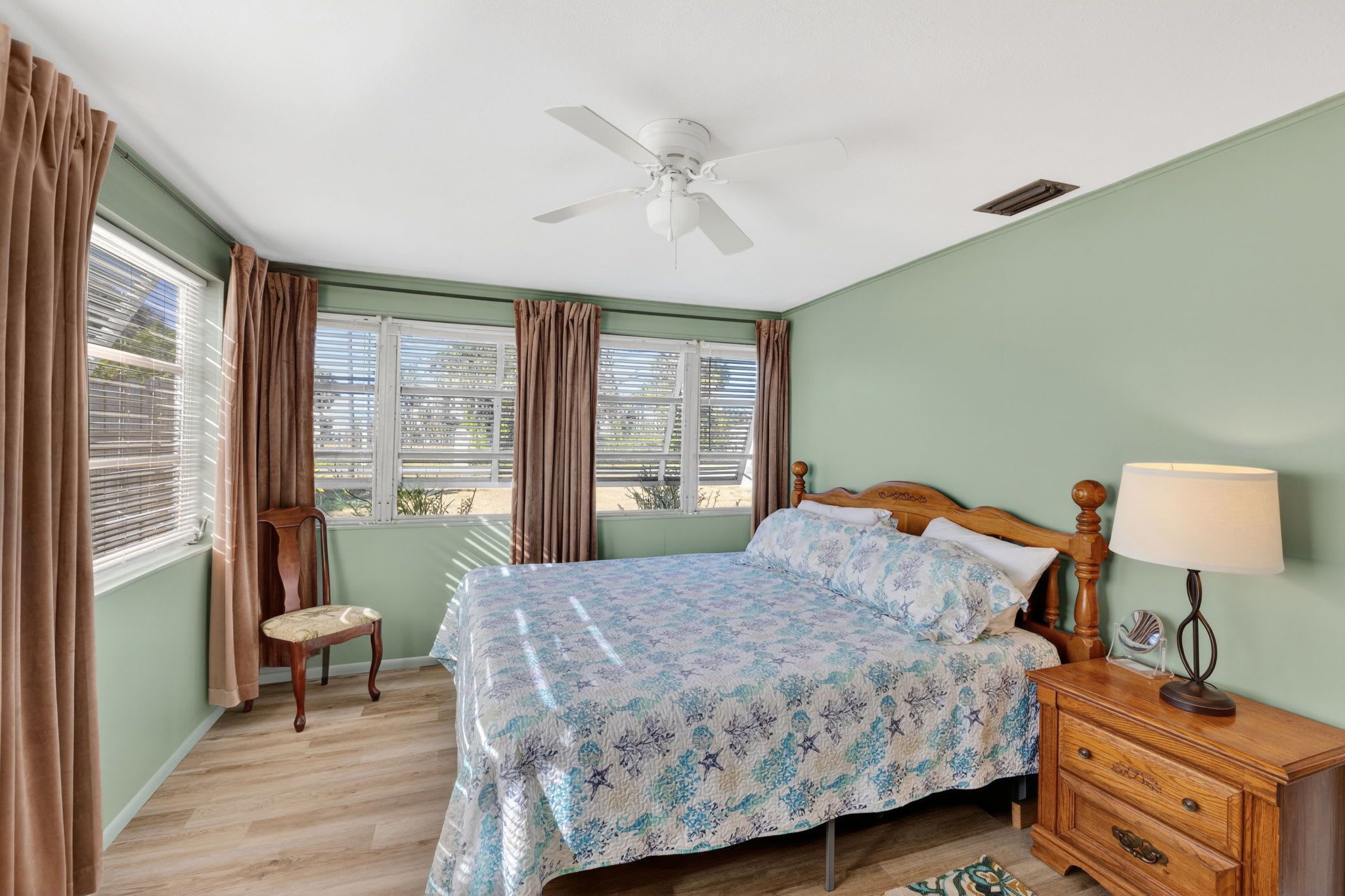 A bedroom with a bed, a chair, a nightstand, a lamp, and a ceiling fan.