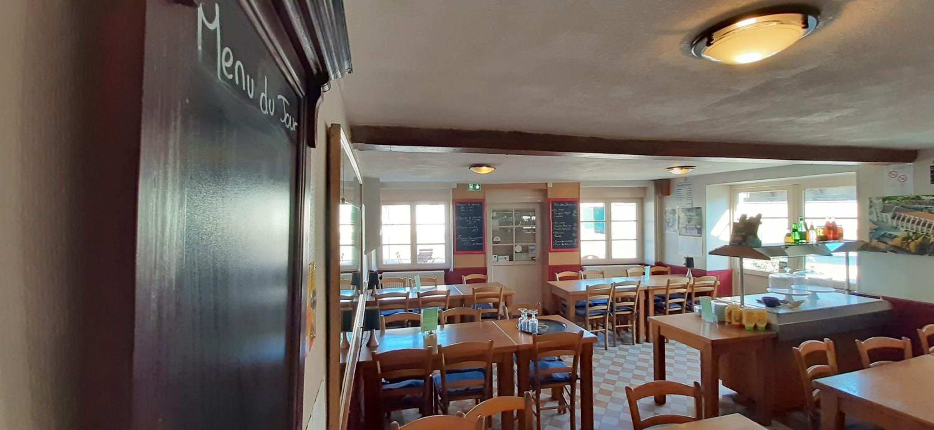 A restaurant interior with wooden tables and chairs, a chalkboard menu, and a view of the street outside.