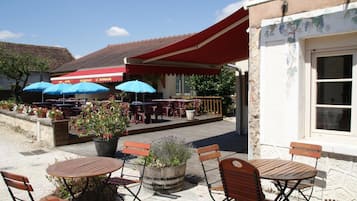 An outdoor seating area with tables and chairs, umbrellas, and potted plants.