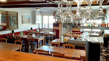 L’intérieur d’un restaurant, avec des tables et des chaises en bois, des luminaires suspendus et un comptoir où sont exposés divers articles.