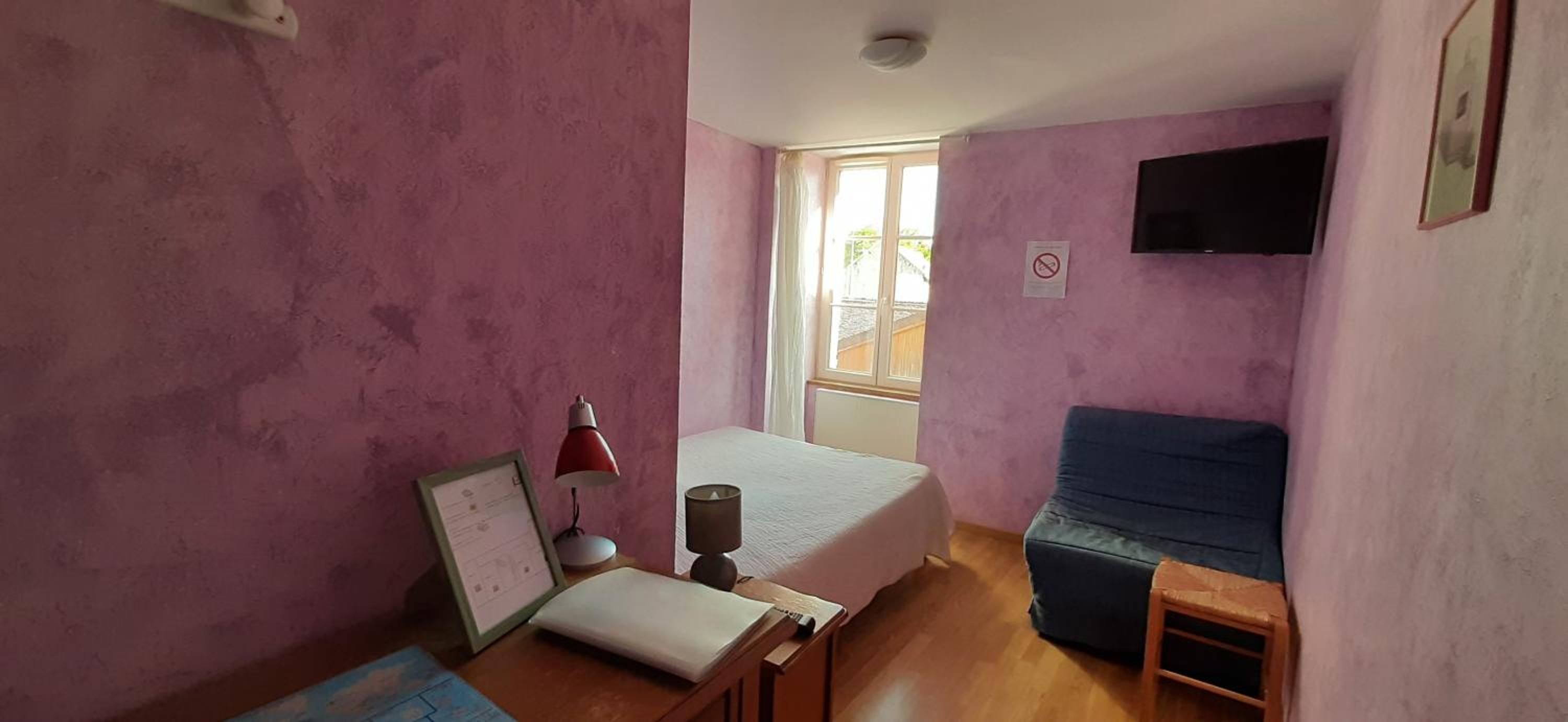 Une chambre à coucher avec un lit, un bureau avec une lampe, une fenêtre et un téléviseur fixé au mur.