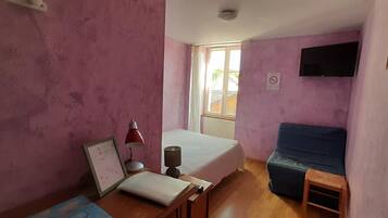 Une chambre à coucher avec un lit, un bureau avec une lampe, une fenêtre et un téléviseur fixé au mur.