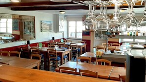 Interior de restaurant amb taules i cadires de fusta, vidrieria penjant i una barra amb diversos objectes.