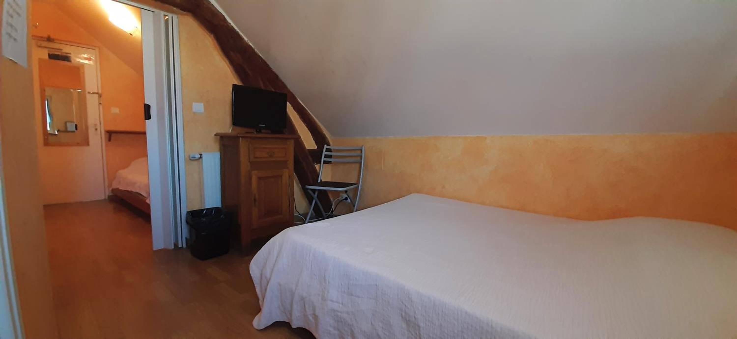 A bedroom with a bed, a television on a wooden cabinet, and a chair.