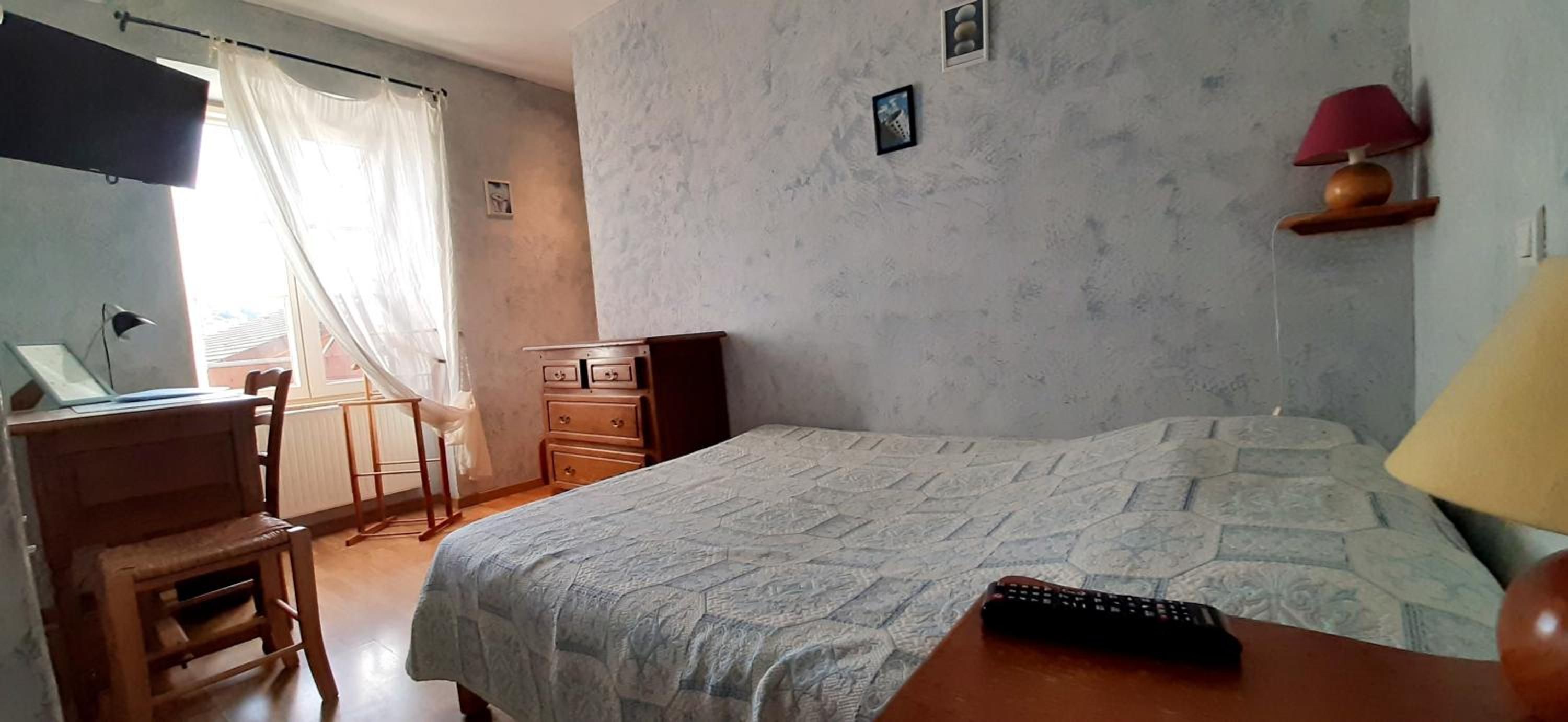 Une chambre à coucher avec un lit, un bureau, une chaise, une lampe et une fenêtre avec des rideaux.