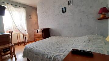 Une chambre à coucher avec un lit, un bureau, une chaise, une lampe et une fenêtre avec des rideaux.