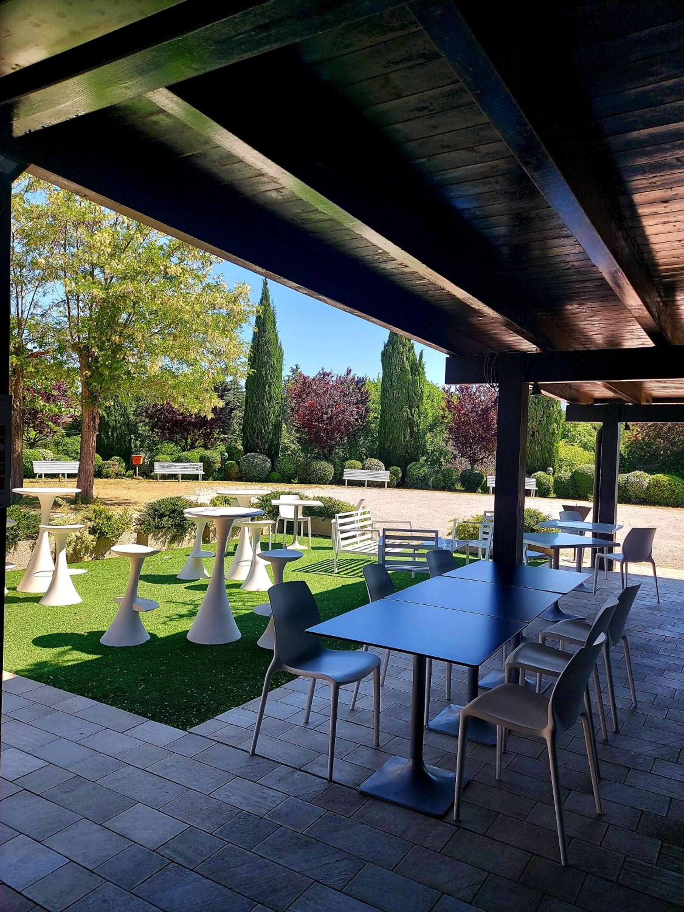 Un patio exterior con mesas y sillas, rodeado de follaje y árboles.