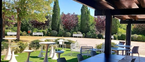 An outdoor patio with tables and chairs, surrounded by greenery and trees.