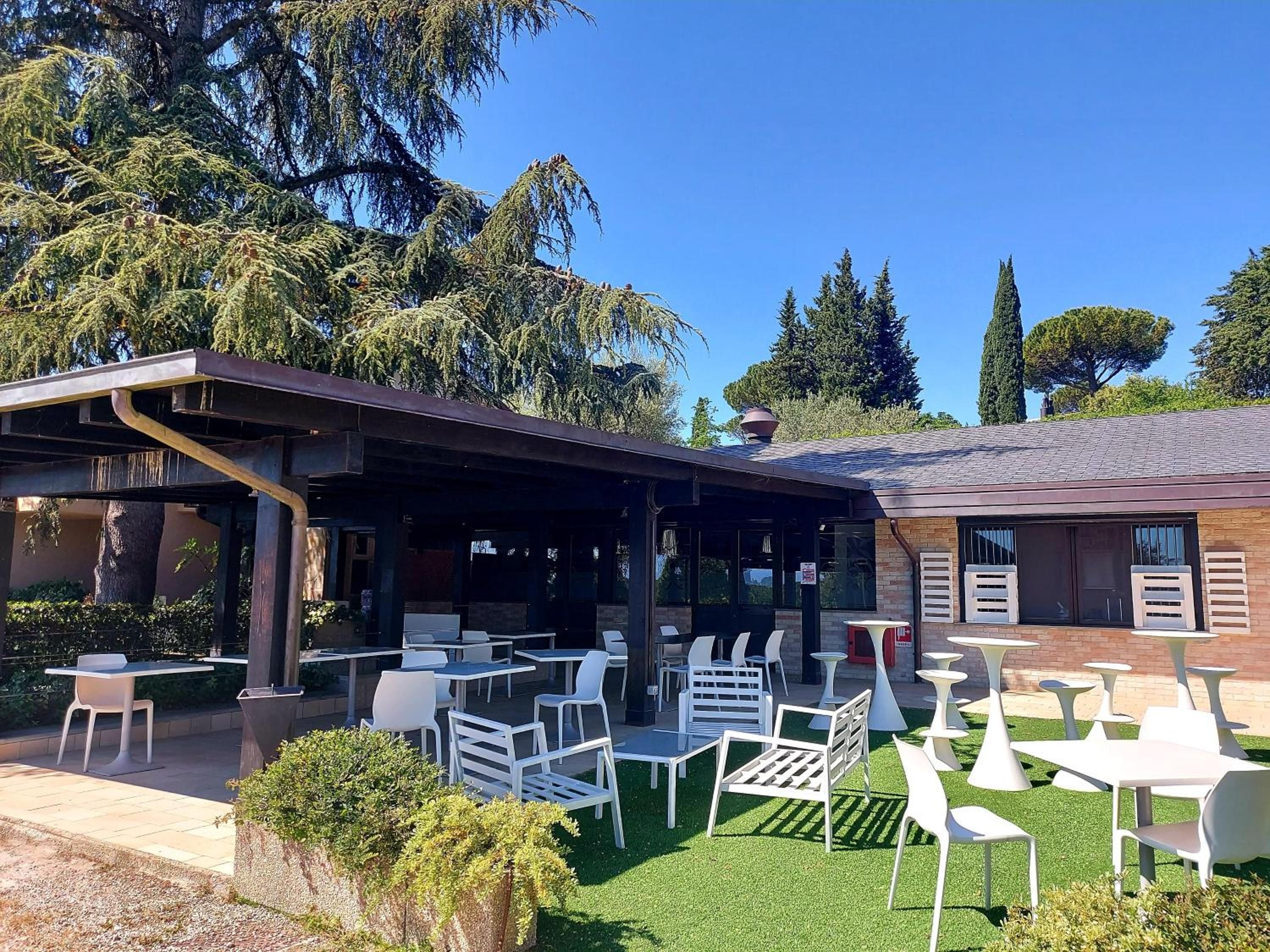 An outdoor patio area with tables and chairs, surrounded by greenery and trees.