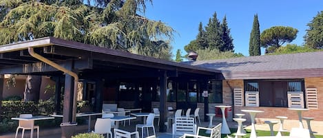 Un patio al aire libre con mesas y sillas, rodeado de follaje y árboles.