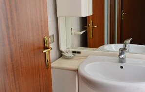 Een badkamer met een houten deur, een wit wastafelmeubel en een spiegel.