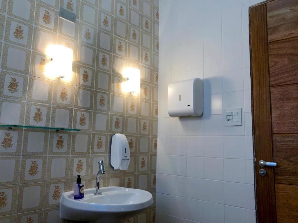 Casa de banho com lavatório, duas luzes na parede, dispensador de sabonete e porta de madeira.