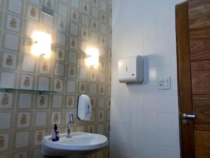 Casa de banho com lavatório, duas luzes na parede, dispensador de sabonete e porta de madeira.
