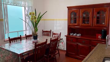 Uma área de refeições com uma mesa posta para quatro pessoas, rodeada por cadeiras de madeira. Um vaso com flores amarelas está sobre a mesa.