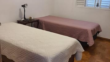 Quarto com duas camas, mesa de cabeceira, abajur e janela com persianas.
