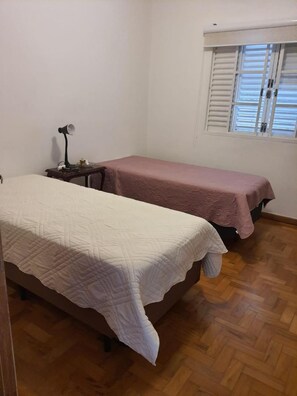 Quarto com duas camas, mesa de cabeceira, abajur e janela com persianas.