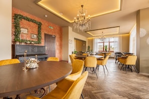 Uma sala de jantar com mesas redondas e cadeiras amarelas, lareira e um candelabro.