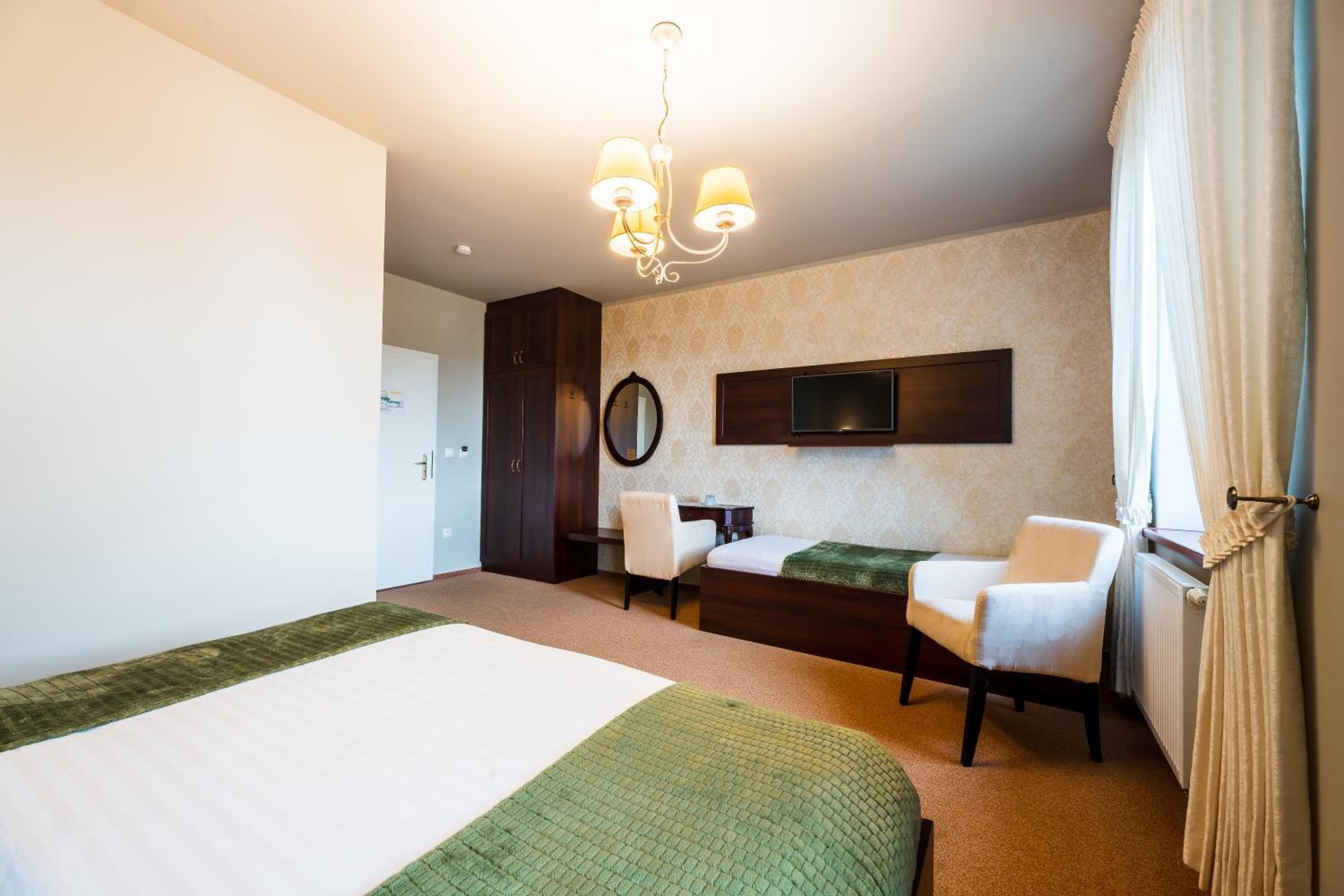 A hotel room with a bed, two chairs, a desk, a television, and a chandelier.