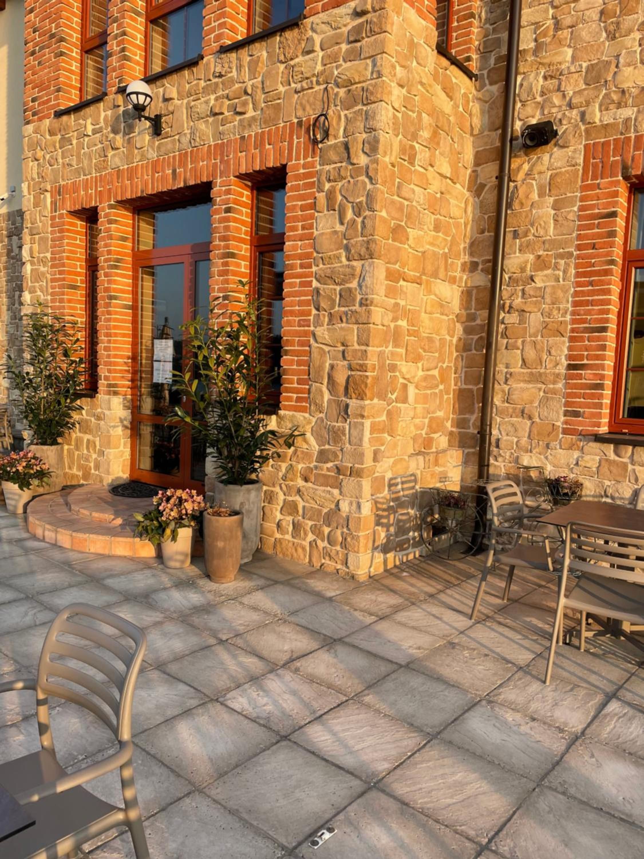 A stone building with a brick facade, outdoor seating area, and potted plants.