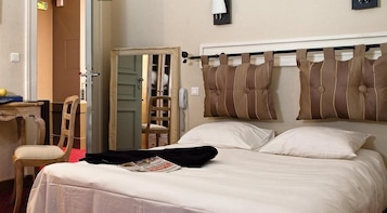 A hotel room with a bed, a chair, a desk, a mirror, and a wardrobe.