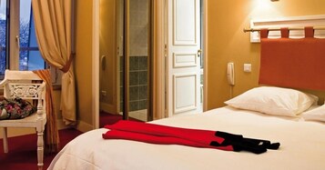 Habitación de hotel con cama, una silla, perchero y puerta que da a un baño.