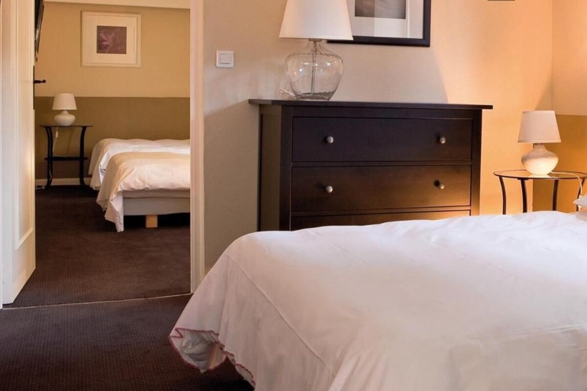 Una habitación de hotel con una cama grande, un aparador, dos mesitas de noche y una lámpara.
