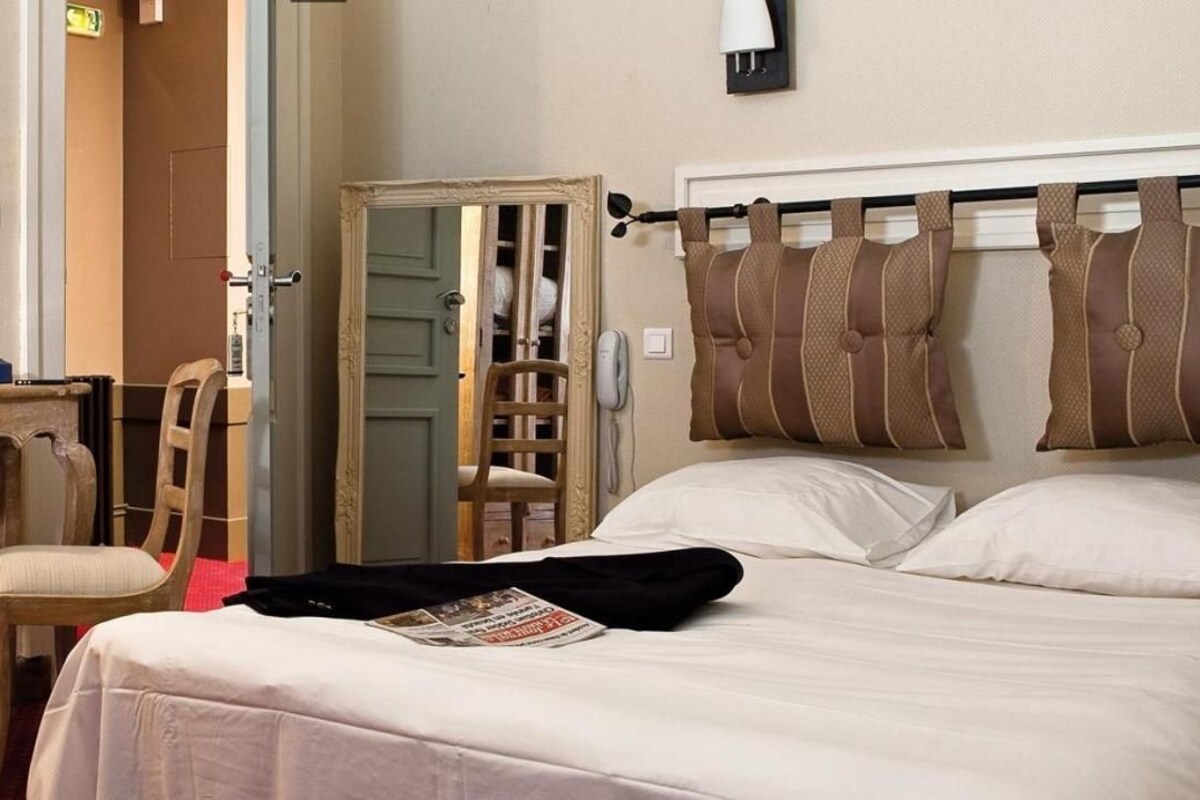 Una habitación de hotel con cama, una silla, un escritorio, un espejo y un armario.