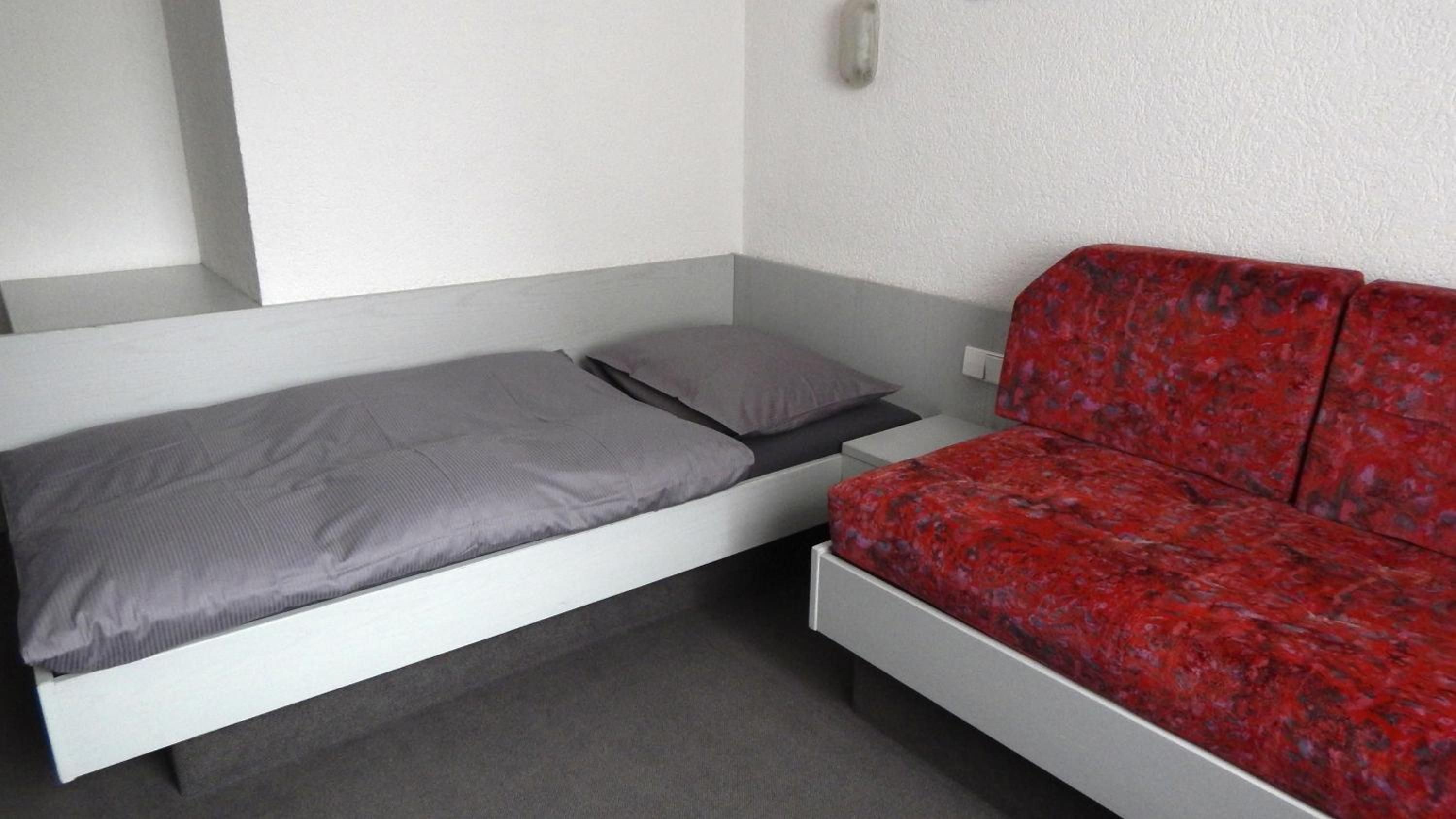 Een kamer met een bed, een rode bank en een wandlamp.